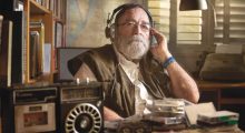A bearded man with headphones on sitting at a desk