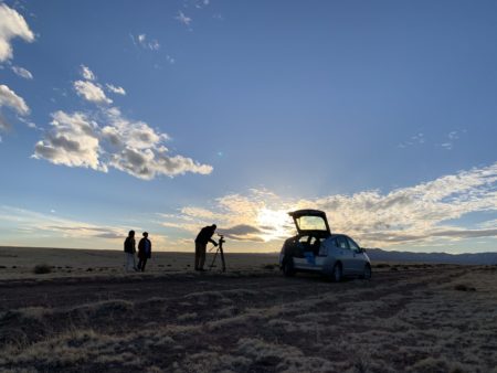 A hatchback car in the desert and three people shooting a movie