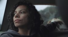 A dark haired woman peering out a car window