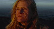 A middle-aged woman with sun-parched skin and blonde hair outdoors looking into the distance