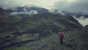 A wide shot of a man walking in a mountainous plain with clouds overhead