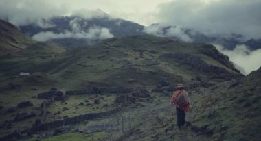 A wide shot of a man walking in a mountainous plain with clouds overhead