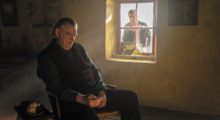 An elderly Irish man named Colm (Brendan Gleeson) sits in a chair next to a window. His younger friend Pádraic (Colin Farrell) stares at him through the window. They do not make eye contact.