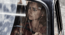 A woman behind the wheel of her car is captured through the reflective glass pane of a windshield.