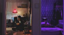 A woman sits on the floor of her apartment eating out of a bowl.