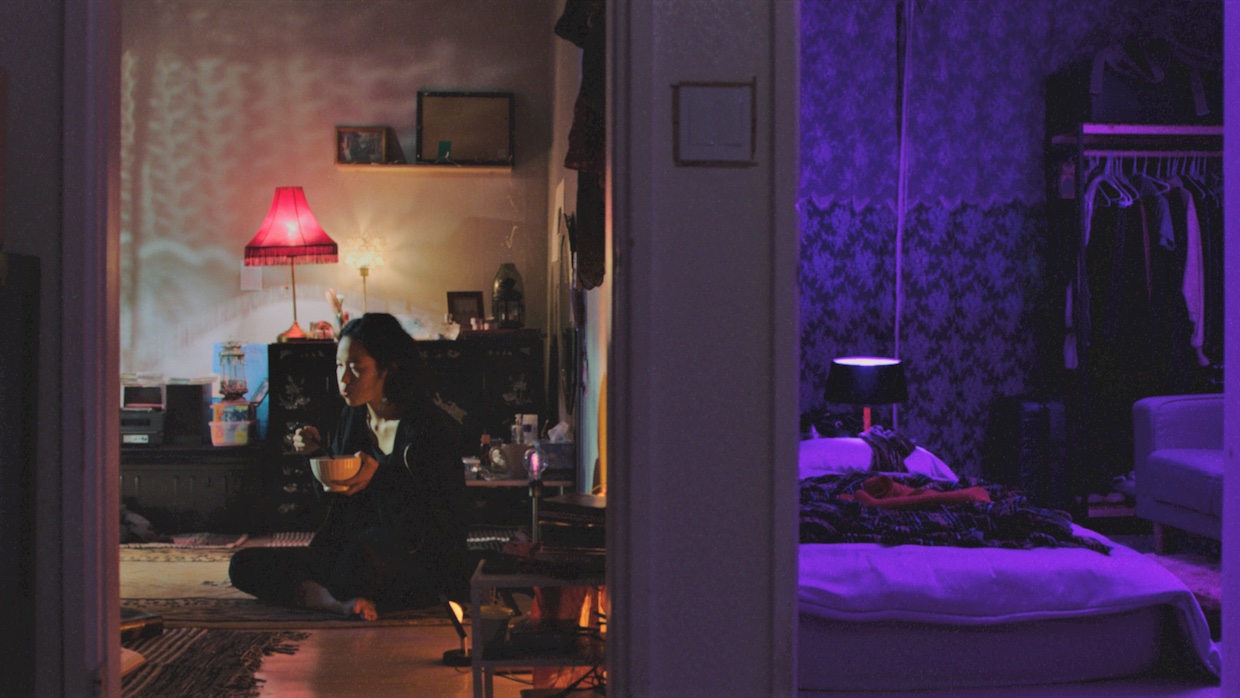 A woman sits on the floor of her apartment eating out of a bowl.