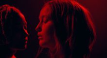 Two girls stand with their faces inches apart, completed drenched in red light.