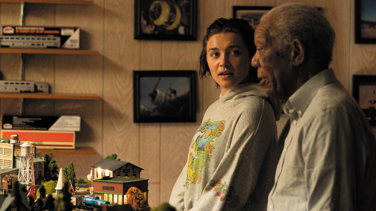 A woman with short brown hair and an elderly Black man stand side by side observing a model train display.