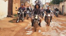 A group of young people ride their motorcycles through damp streets in a Brazilian town.