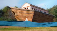 A giant, wooden arc sits in the middle of a green field. A large blue tarp simulates the look of water below it.