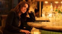A woman with long brown hair sits at a bar and leans her head on her left hand.