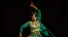 A teenage girl in traditional, green Desi formal wear strikes a pose as she performs a traditional dance.