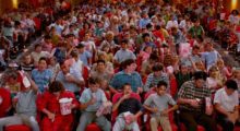 A theater is packed, young people and kids sit on the bright red velvet seats and throw popcorn, stare at the screen and cheer.