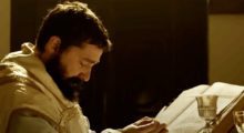 A priest dressed in white Catholic robes as he looks down at a holy bible.