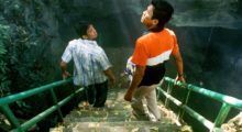 Two men descend down a steep concrete staircase that leads into a Thai cave.