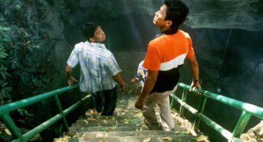 Two men descend down a steep concrete staircase that leads into a Thai cave.