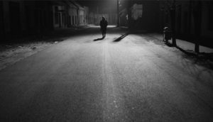 A black and white shot of a man walking down a vast, desolate street.