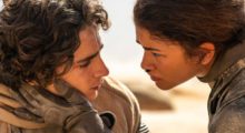 A woman (Zendaya) in futuristic protective sci-fi attire caresses the face of a man (Timothée Chalamet) amid a barren desert landscape.