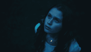 A young girl stands outside and gazes at the sky. She is bathed in pale blue moonlight.