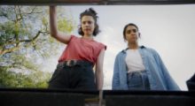Two woman peer into a trunk, we look up at them as they gaze inside.