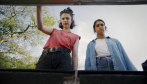 Two woman peer into a trunk, we look up at them as they gaze inside.