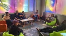 A diverse group of people sit in neon green beanbag chairs in a circle in a room, the window reads PAM CUT: Center for an Untold Tomorrow.