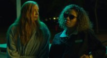 A woman with long, straight blonde hair stands next to a woman with shoulder-length curly brown hair.