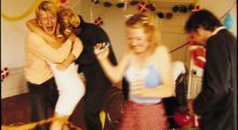 A handful of young, predominantly blonde young Danish people dance at a party.