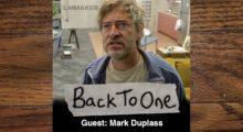 An image of actor and filmmaker Mark Duplass, who wears a beige t-shirt, grey hoodie and scowls while looking off to the side.
