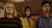 Three young people, one with long platinum blond hair, one with a brown bob and one with cropped dark hair all stand next to each other in a hallway.