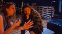 Two young women with brown hair kneeling on a porch at night.