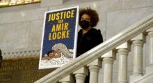 Young man in a black hoodie holds up a poster that reads, "Justice for Amir Locke" at demonstration
