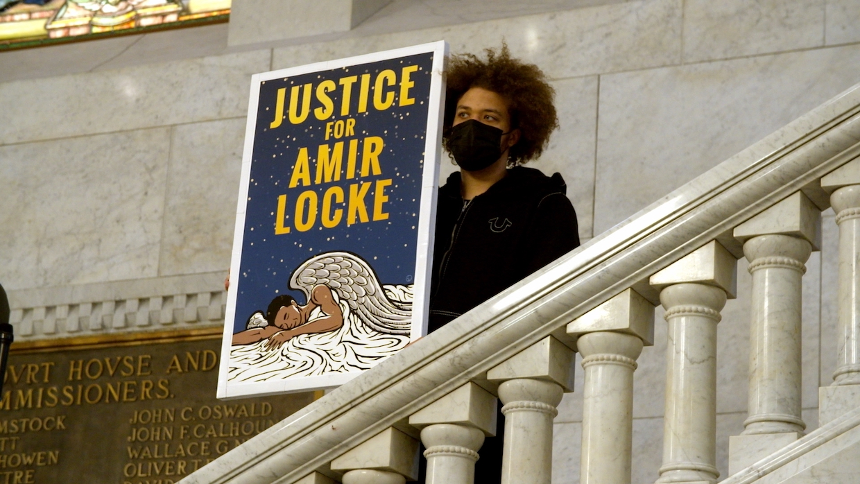 Young man in a black hoodie holds up a poster that reads, "Justice for Amir Locke" at demonstration
