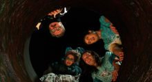 Four people peer down a well at night.