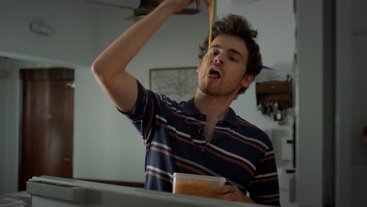 A man eats spaghetti out of his hands while holding a Tupperware container.