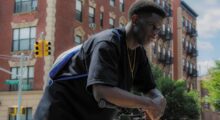 A black teenage boy hunches over a scooter on a street.