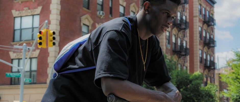 A black teenage boy hunches over a scooter on a street.