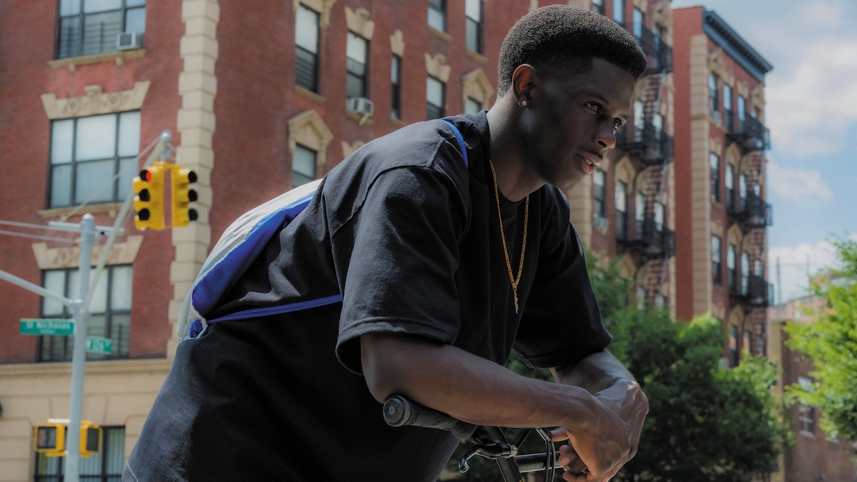 A black teenage boy hunches over a scooter on a street.