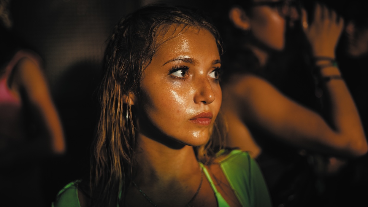 A young woman in a green top stands in a crowd.