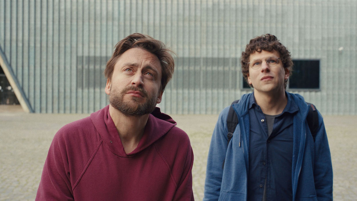 Two white men, one wearing a red hoodie and one wearing a blue zip-up, gaze upward.