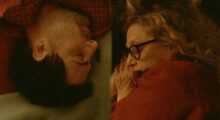 A man sleeps opposite an older woman on a mattress, both their heads facing in opposite directions.