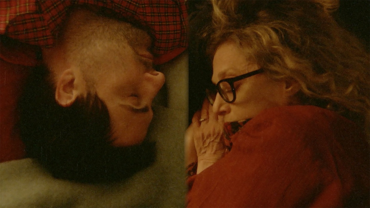 A man sleeps opposite an older woman on a mattress, both their heads facing in opposite directions.