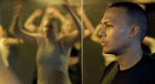 A Hispanic man looks to the left in the foreground, while in the background a woman is seen flexing in a mirror.