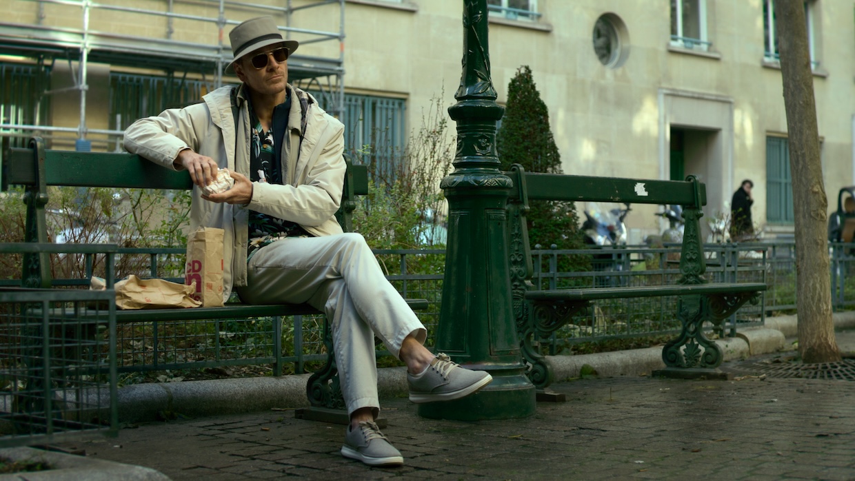 A man with a paper takeout bag from McDonald's sits on a park bench in daylight.