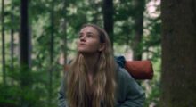 A white teenage girl with a camping backpack looks up in the forested Pacific Northwest.