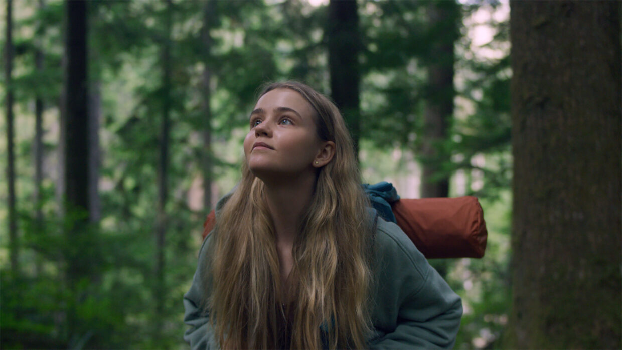 A white teenage girl with a camping backpack looks up in the forested Pacific Northwest.