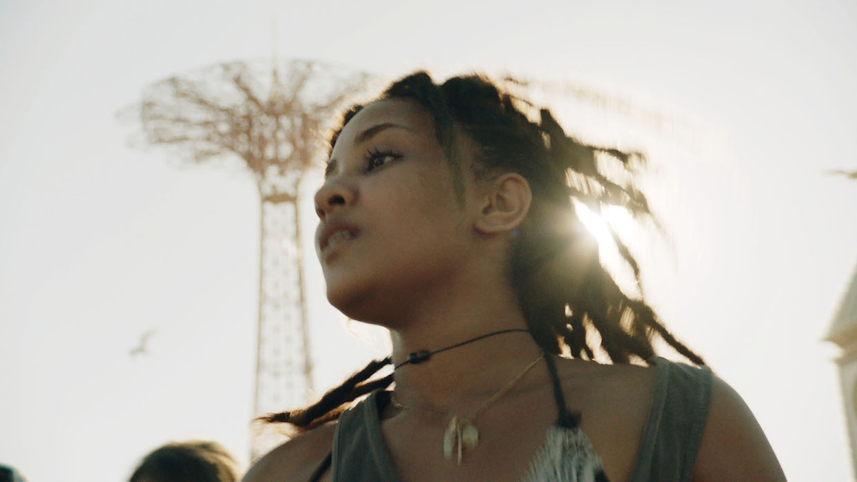 A young Black woman stands in front of a Coney Island ride.