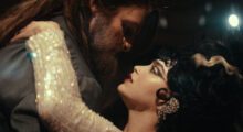 A bearded man and a woman, locked in tight embrace, prepare to kiss.