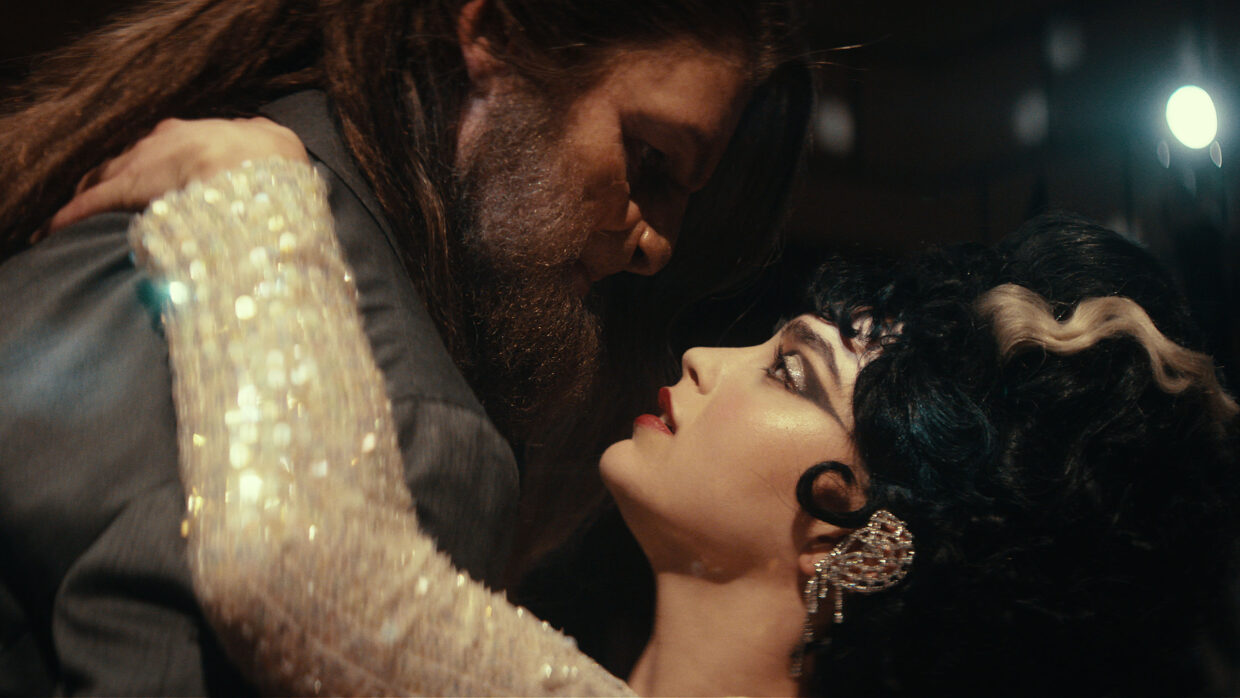 A bearded man and a woman, locked in tight embrace, prepare to kiss.