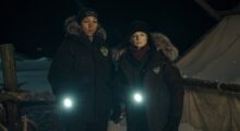 Two women shine their flashlights while standing in a dark, snowy landscape.